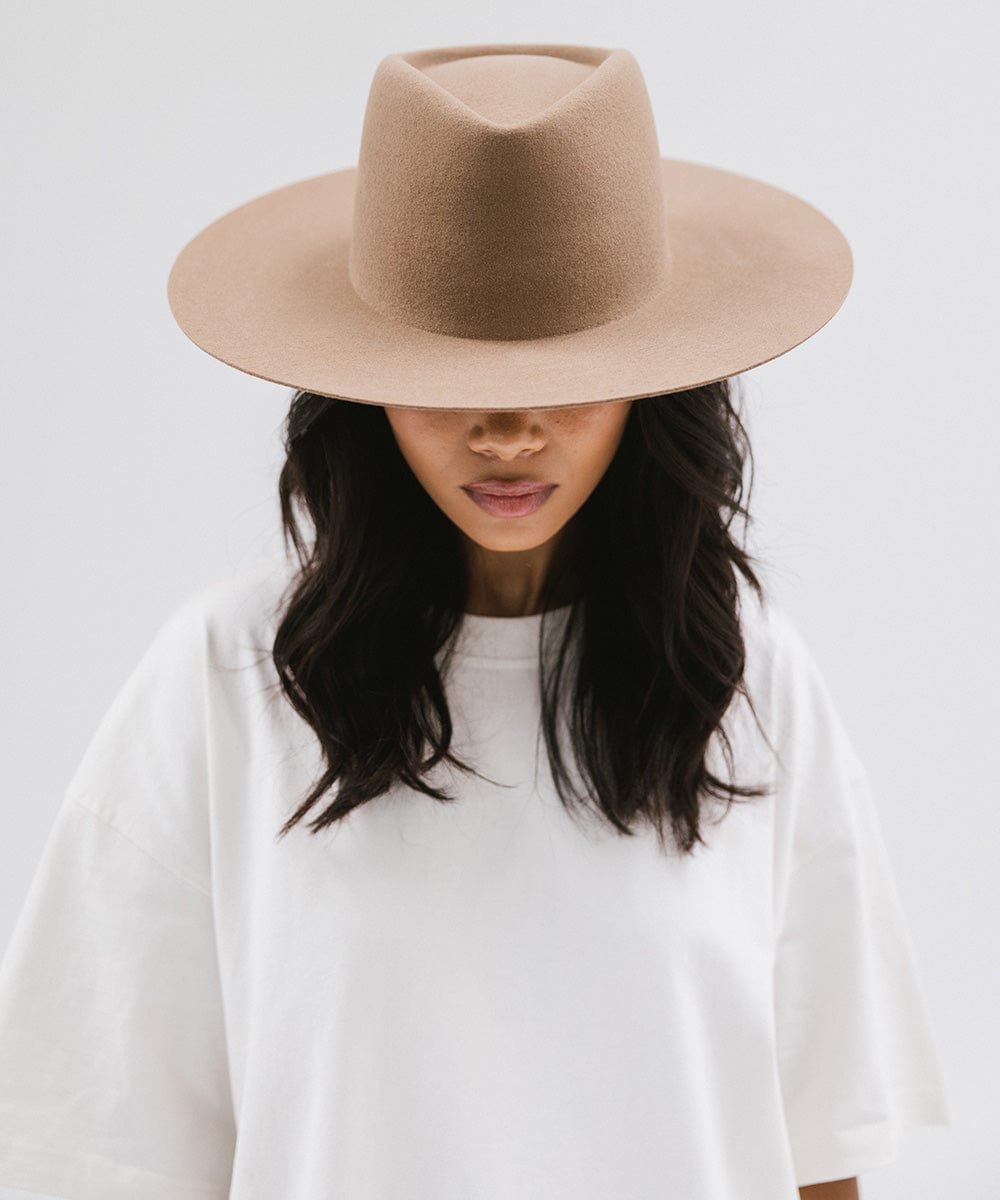 Woman wearing a brown wide brim felt hat with a triangle crown and a white shirt against a white background #color_brown