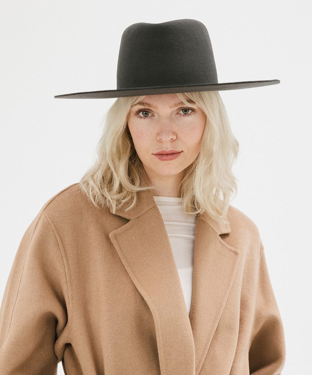 Woman wearing a dark grey wide brim felt hat with a triangle crown and a brown jacket against a white background #color_dark grey