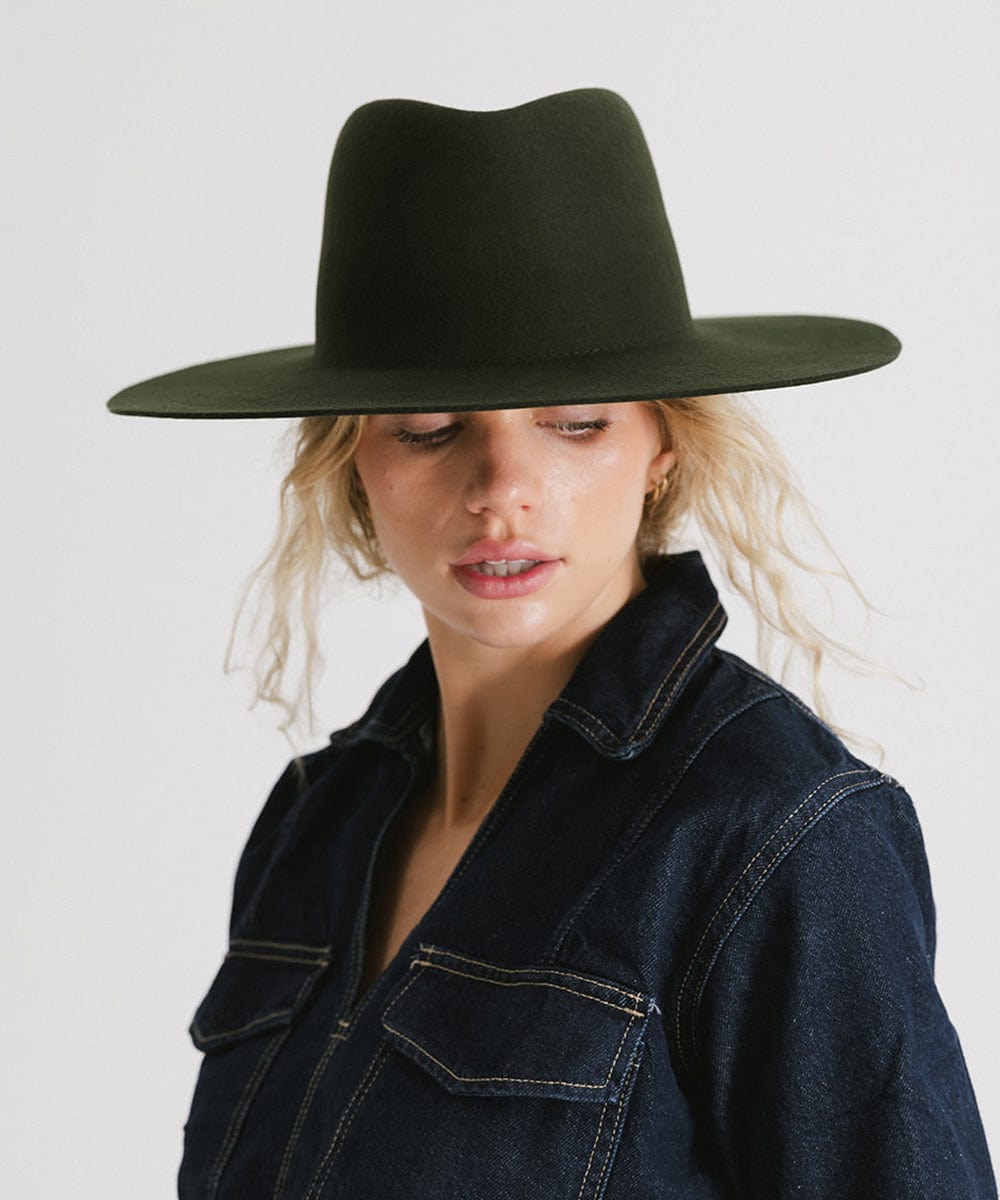 Woman wearing a dark green wide brim felt hat with a triangle crown and a denim jacket against a plain background #color_dark green