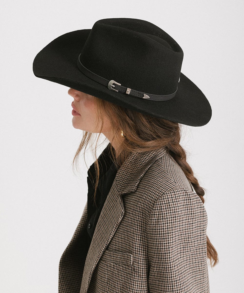 Woman wearing a black cowboy hat with a hat band and a blazer, facing sideways against a plain background #color_black