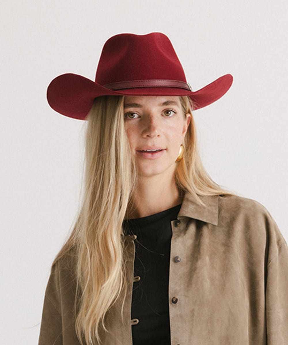 Woman wearing a burgundy cowboy hat with a hat band and a black t-shirt with a beige shirt against a plain background #color_burgundy