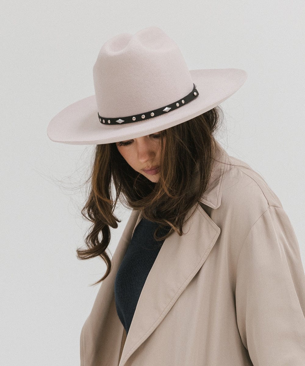 Woman wearing an ivory colored Western hat with a classic cattleman crown and black hat band, and a beige coat, looking down against a plain background #color_ivory