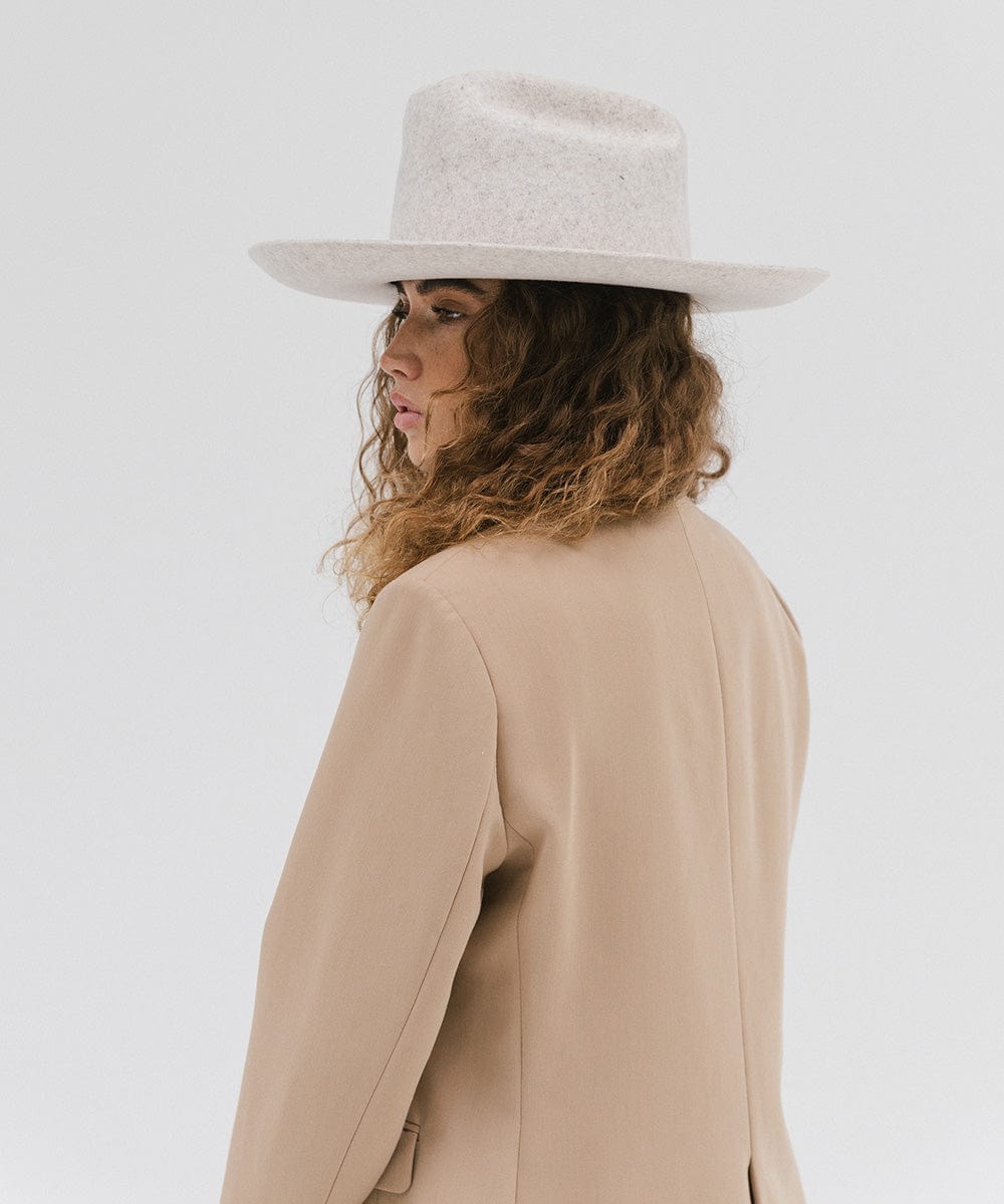 Woman wearing a mix grey colored Western hat with a classic cattleman crown, and a beige coat, facing sideways against a plain background #color_mix grey