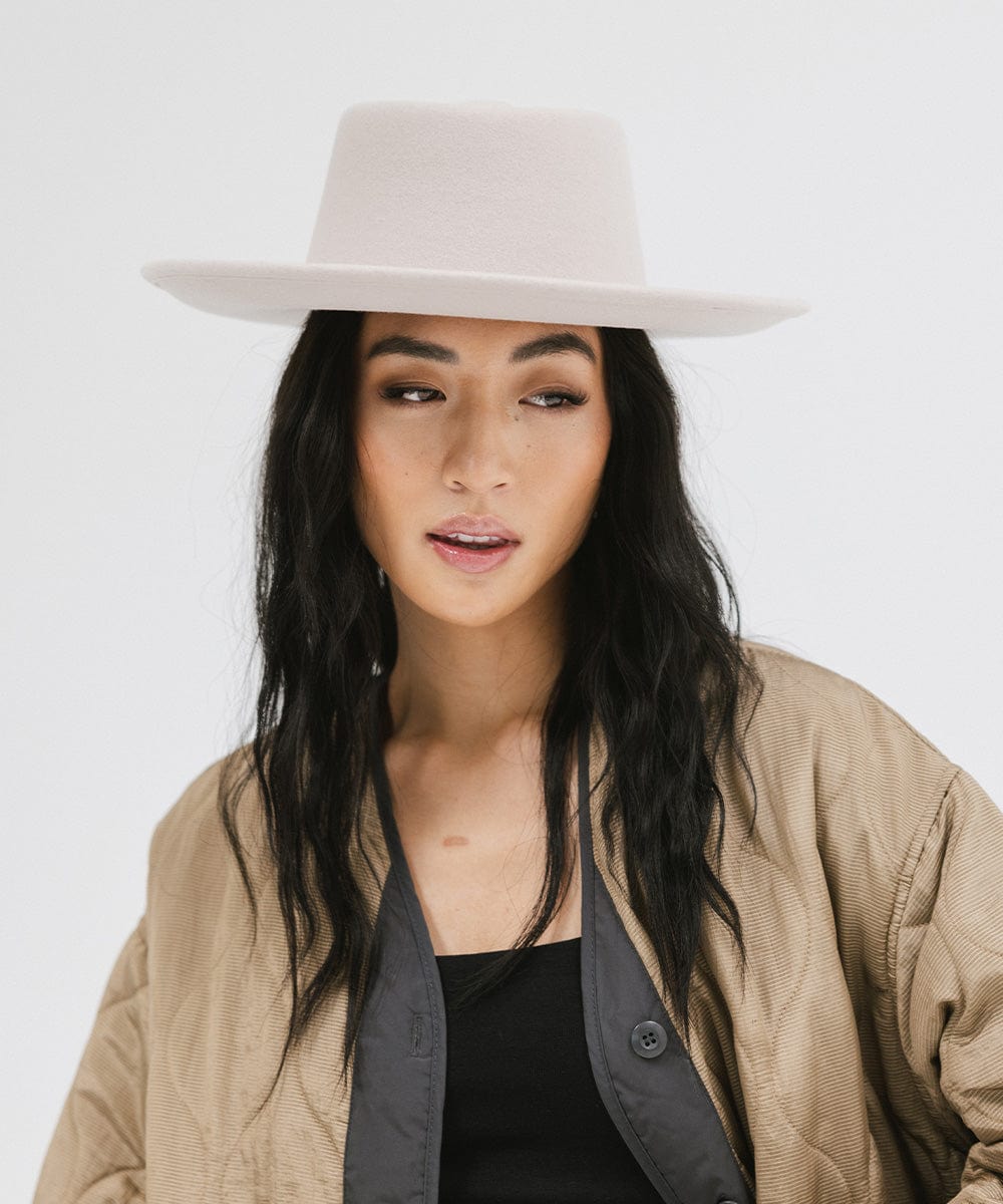 Woman wearing an ivory colored gambler hat and a brown jacket against a plain background #color_ivory