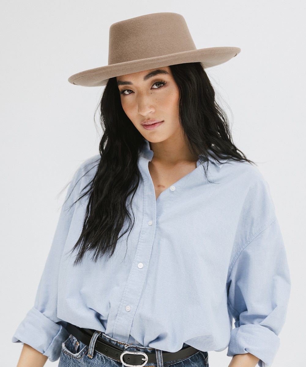 Woman wearing a taupe colored gambler hat and a blue shirt and jeans against a plain background #color_taupe