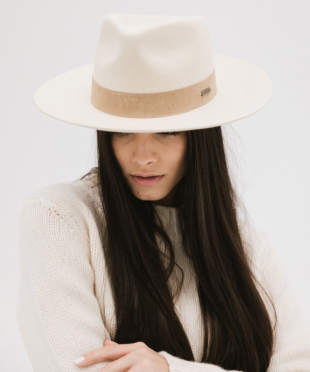 Woman wearing an off white felt fedora hat with a band and a white sweater, posing against a plain background #color_off white