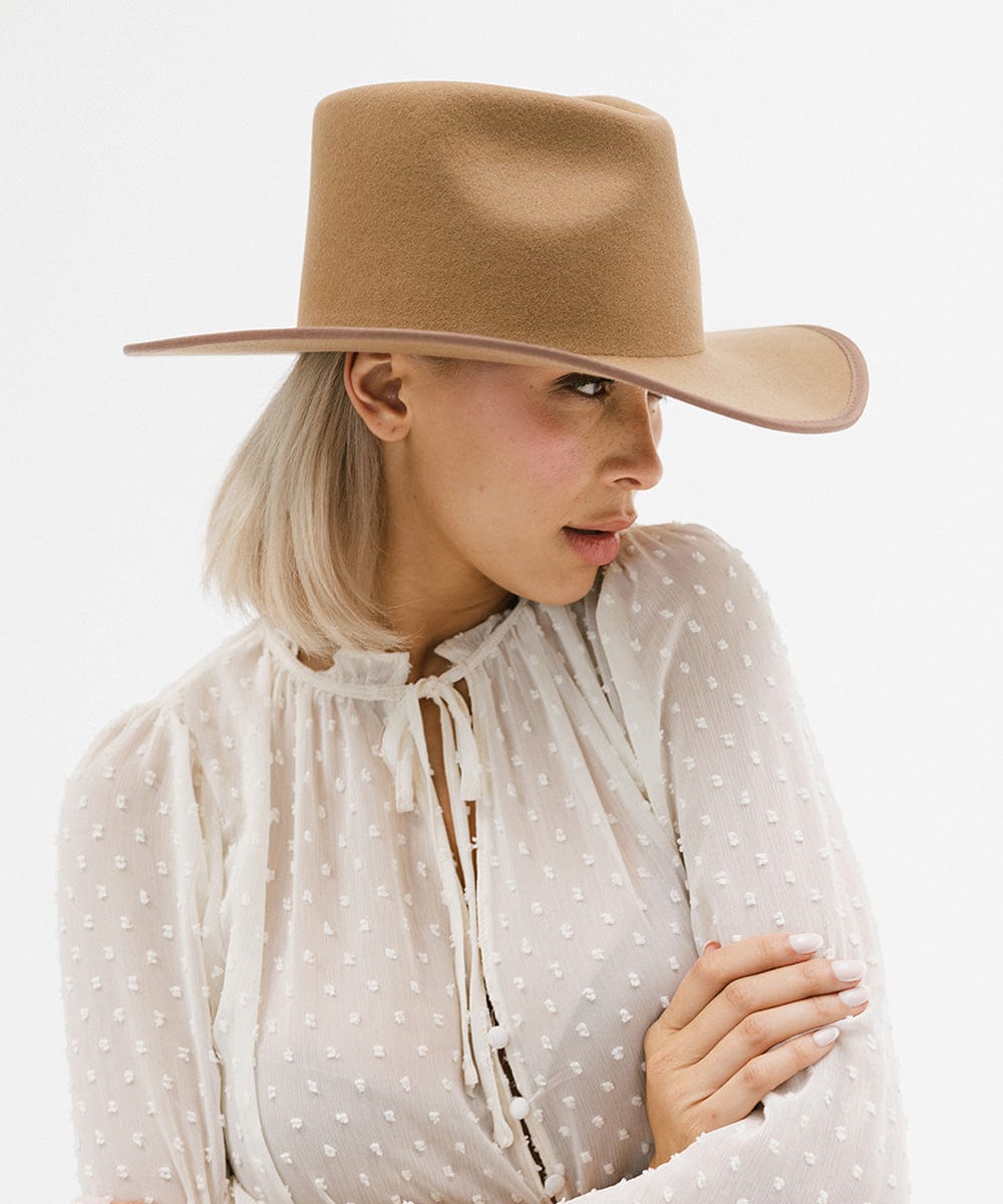 Woman wearing a brown felt western hat and a white top, looking sideways against a white background #color_brown