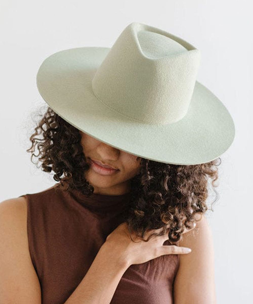 Woman wearing a light green fedora hat and a brown top against a plain background #color_light green