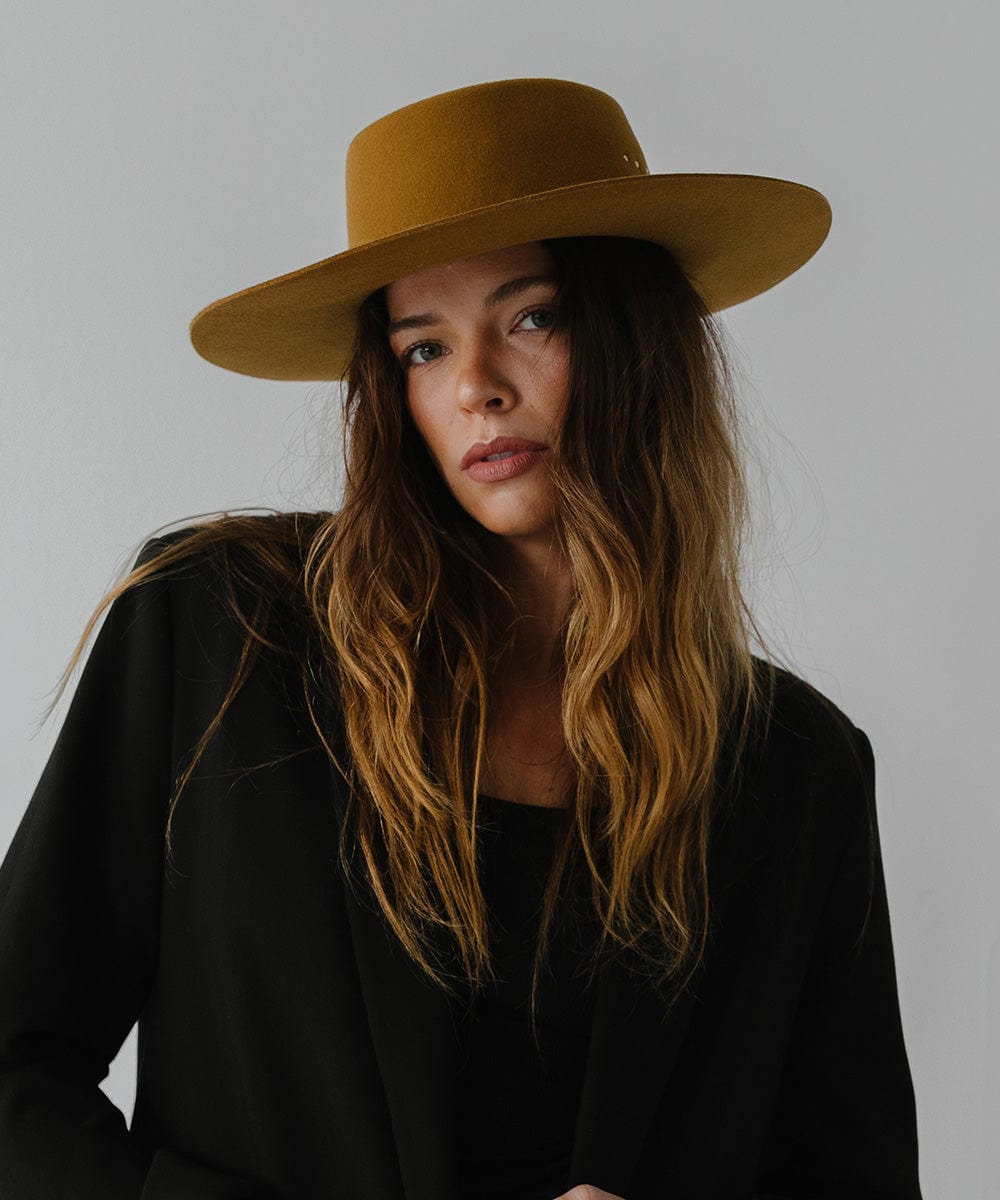 Woman wearing a cinnamon colored boater hat and a black coat against a plain background #color_cinnamon