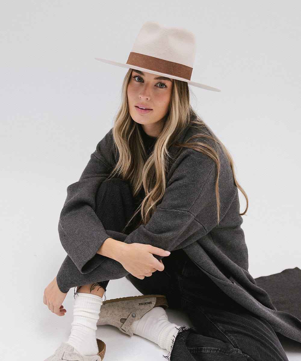Woman wearing an ivory colored fedora hat with a brown band and a dark coat on a white background #color_ivory