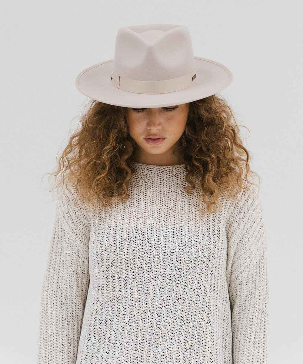 Woman wearing an ivory colored fedora hat with a band and a white knit sweater against a plain background #color_ivory