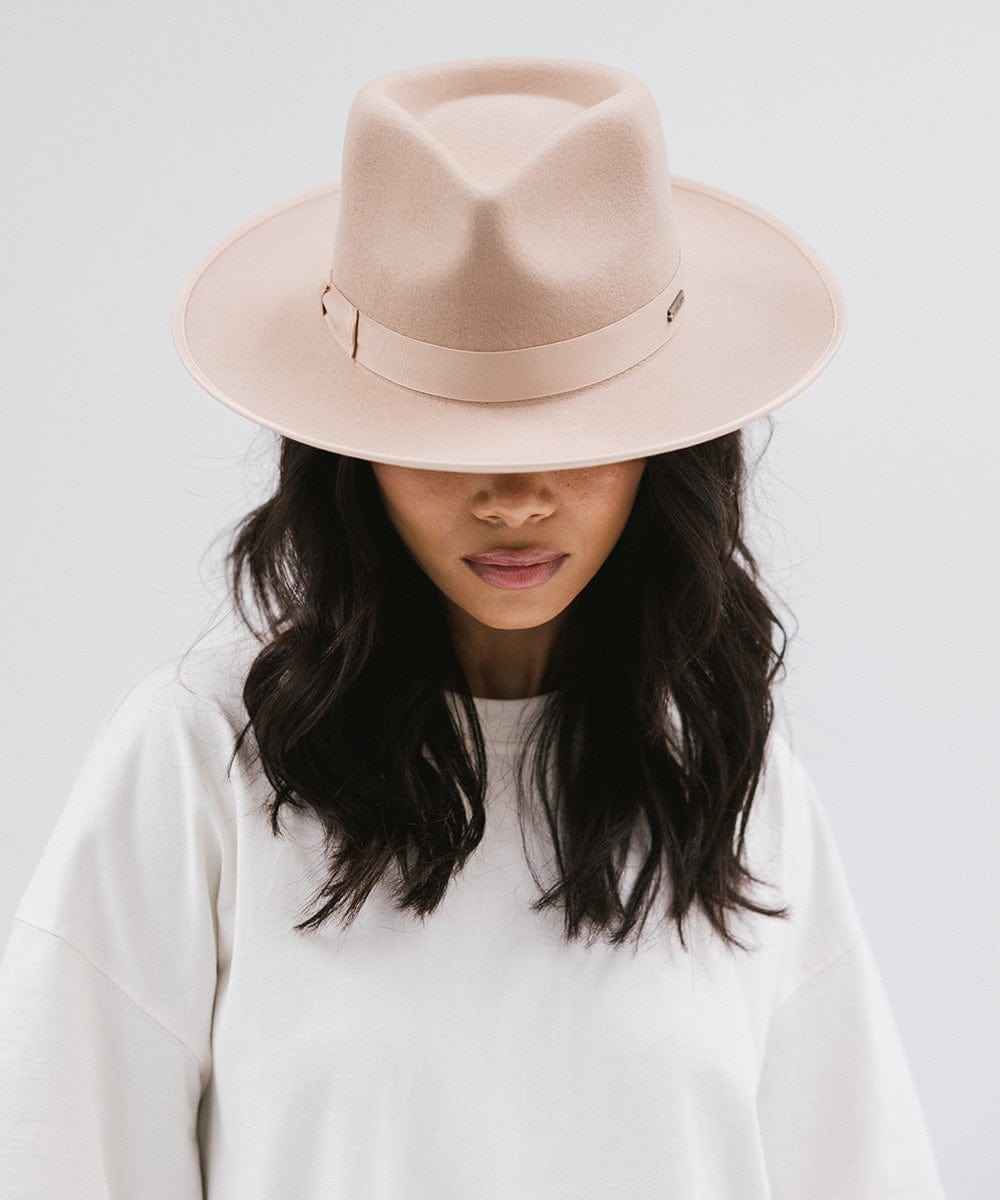 Woman wearing a nude fedora hat with a band and a white t-shirt against a plain background #color_nude