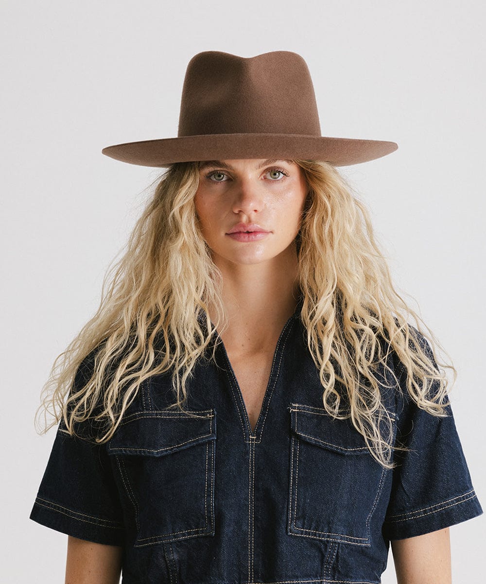 Woman with long blonde hair wearing a chocolate colored Rowan Wide Brim Fedora Hat and a denim shirt against a plain background #color_chocolate