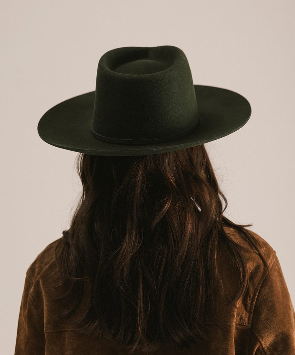 Person wearing a dark green hat and brown jacket with long hair, on a plain background #color_dark green