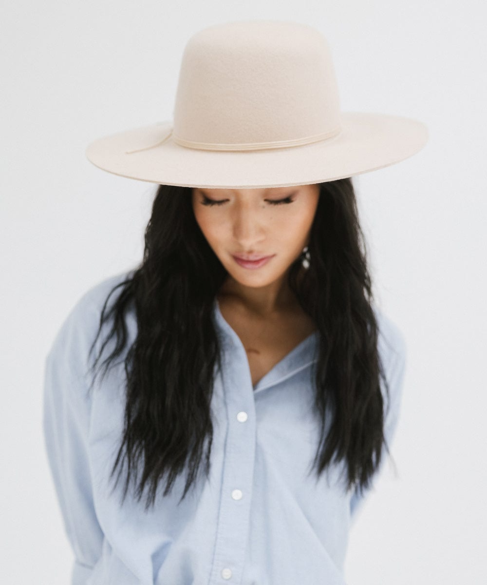 Woman wearing a cream open crown hat with a hat band and a blue shirt against a plain background #color_cream