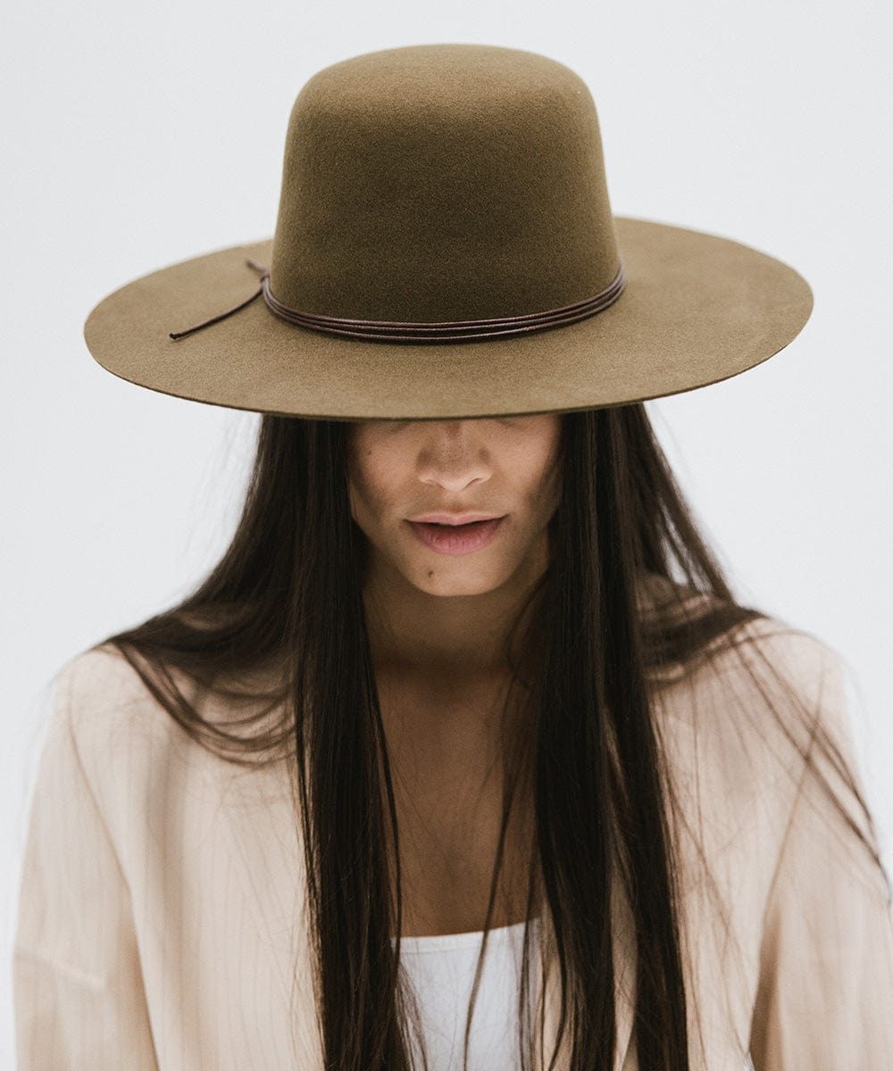 Woman wearing an olive colored open crown hat with a hat band and a cream blazer against a plain background #color_olive