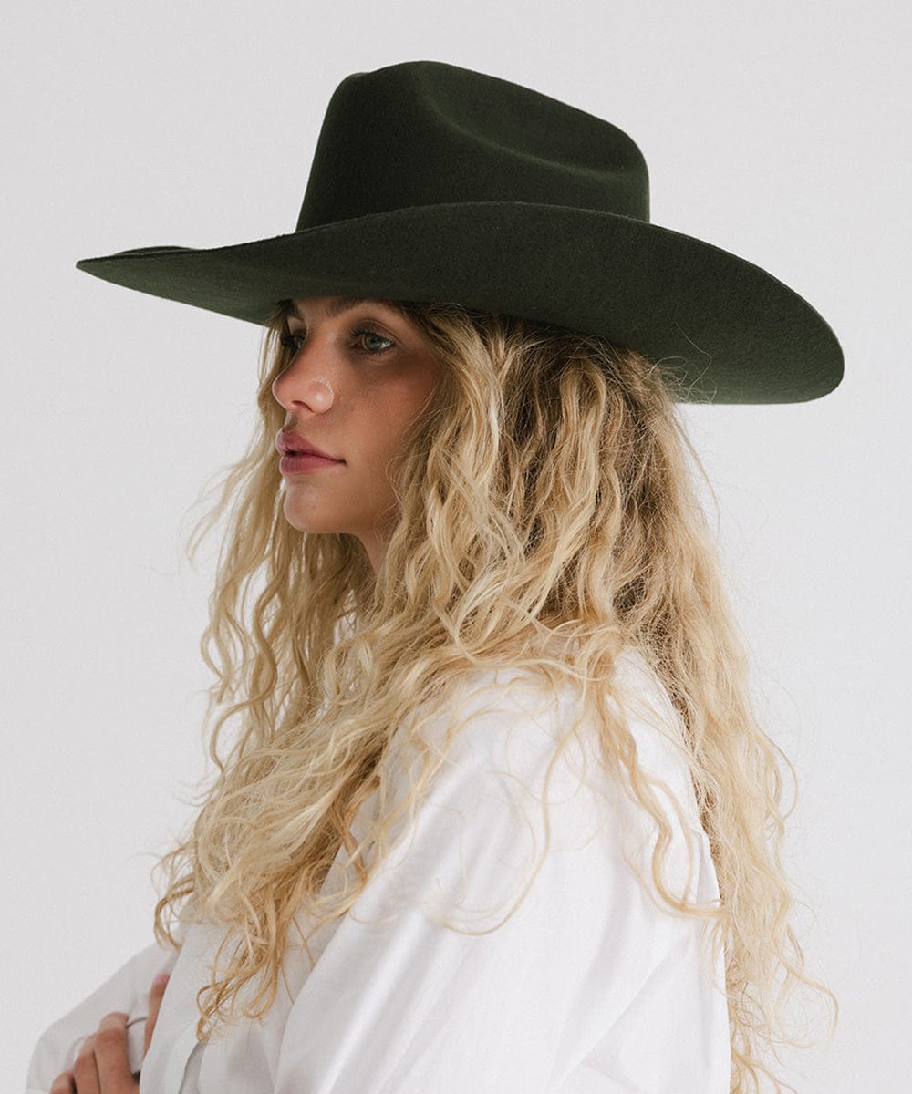 Woman wearing a dark green cowboy hat and a white shirt, facing sideways against a plain background #color_dark green