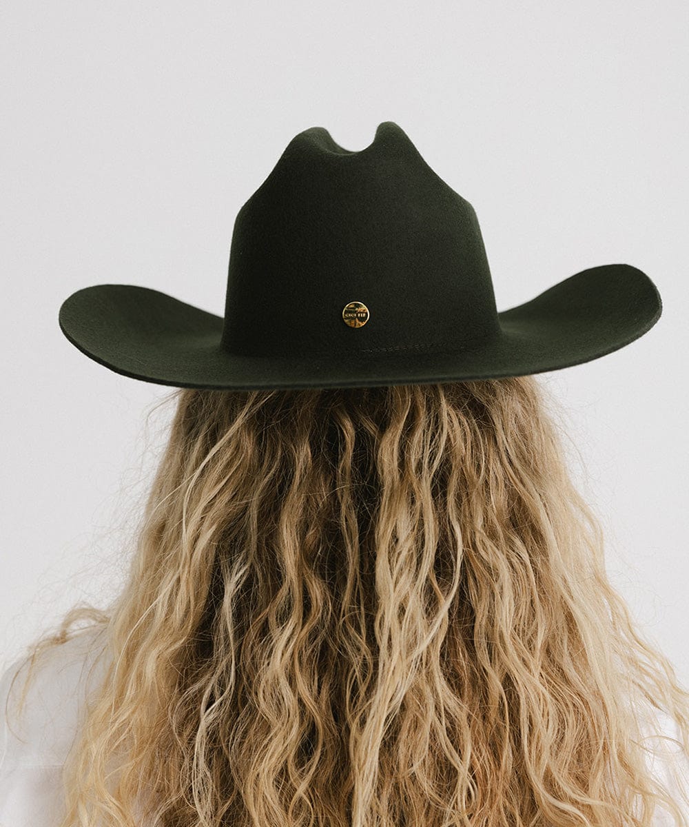 Woman wearing a dark green cowboy hat facing behind against a plain background #color_dark green