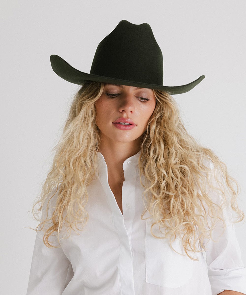 Woman wearing a dark green cowboy hat and a white shirt against a plain background #color_dark green