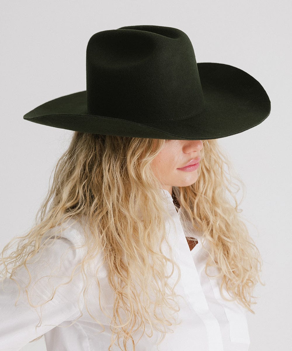 Woman wearing a dark green cowboy hat and a white shirt, looking sideways against a plain background #color_dark green