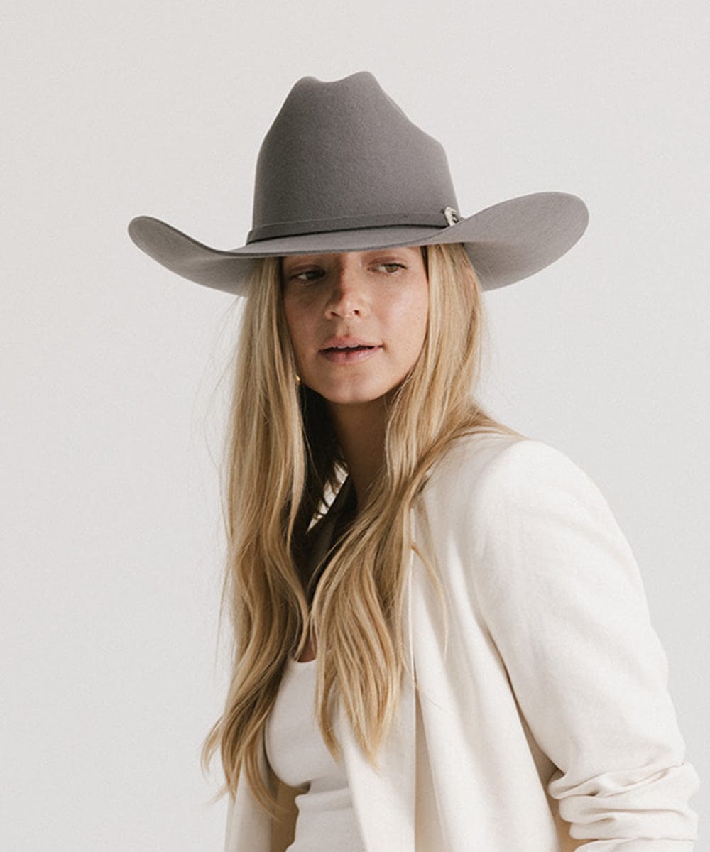 Woman wearing a limited edition stone colored cowboy hat with a hat band and a white blazer against a plain background #color_limited edition stone