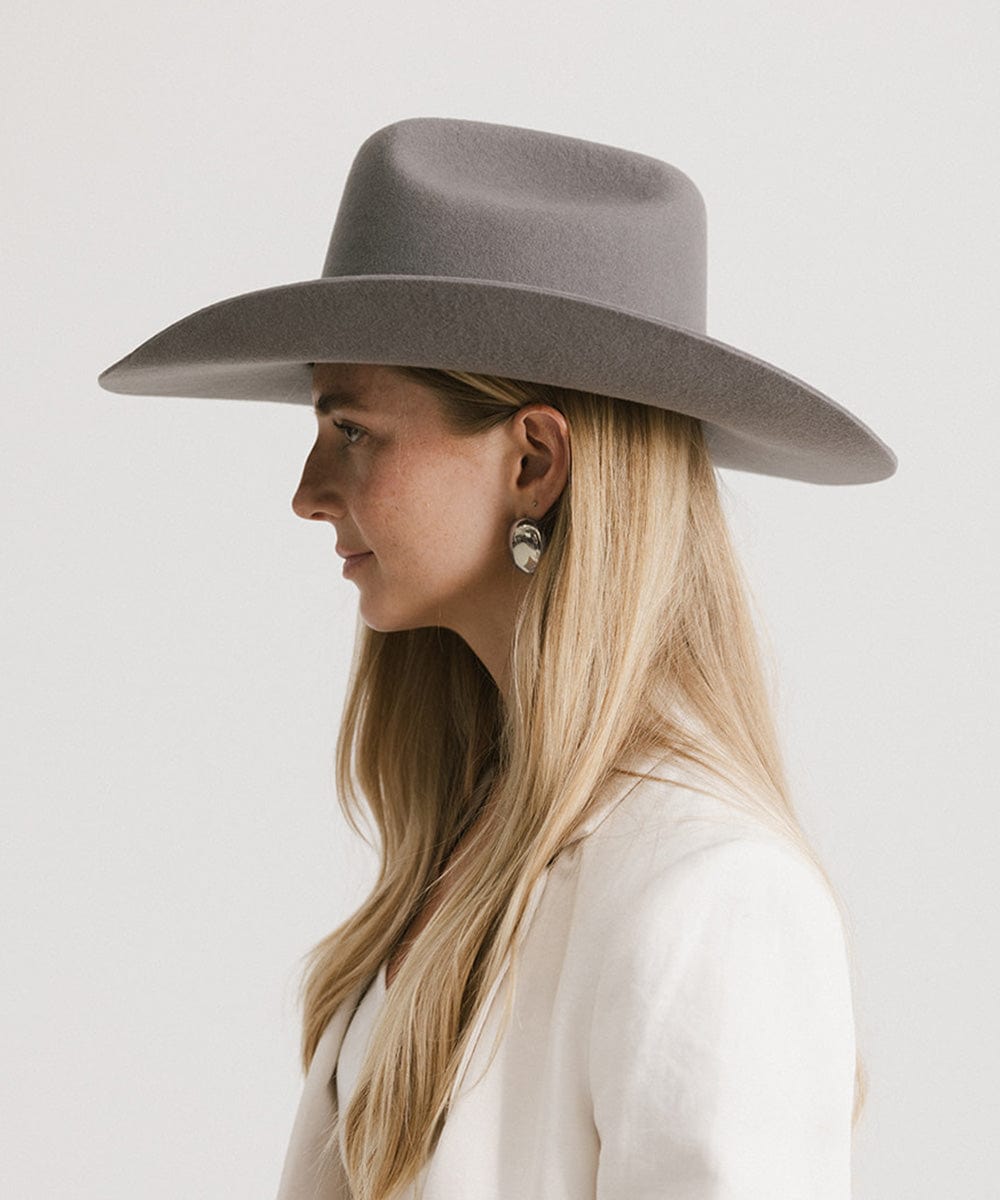 Woman wearing a limited edition stone colored cowboy hat with a hat band and a white blazer against a plain background #color_limited edition stone