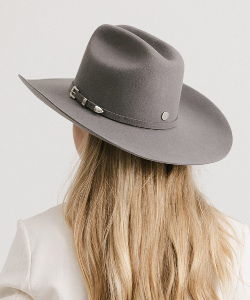 Woman wearing a limited edition stone colored cowboy hat with a hat band and a white blazer, facing behind against a plain background #color_limited edition stone