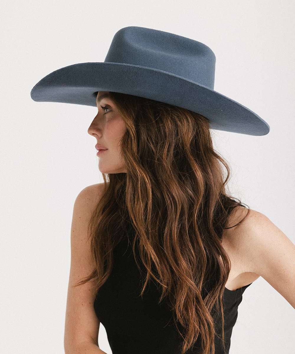 Woman wearing a vintage blue colored cowboy hat and a black top, looking sideways against a plain background #color_vintage blue