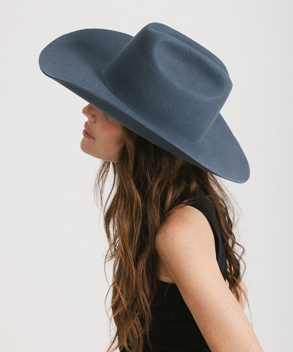Woman wearing a vintage blue colored cowboy hat and a black top, facing sideways against a plain background #color_vintage blue