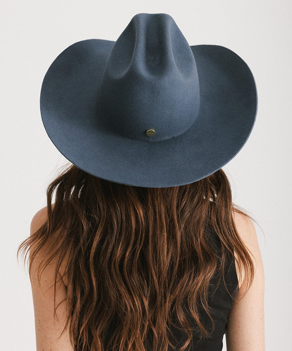 Woman wearing a vintage blue colored cowboy hat and a black top, facing behind against a plain background #color_vintage blue