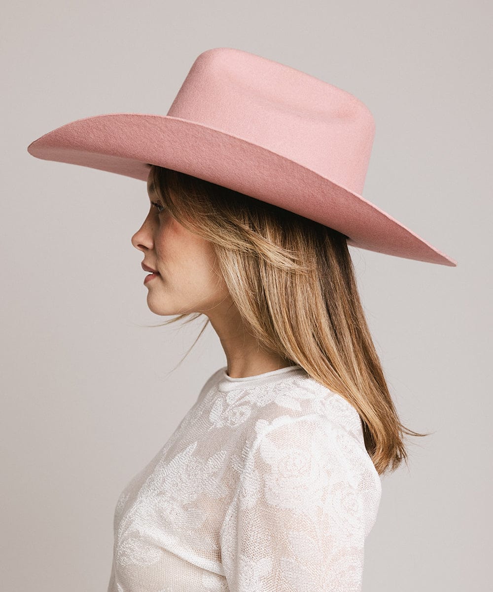 Woman wearing a rose colored cowboy hat and a white t-shirt, facing sideways against a plain background #color_rose