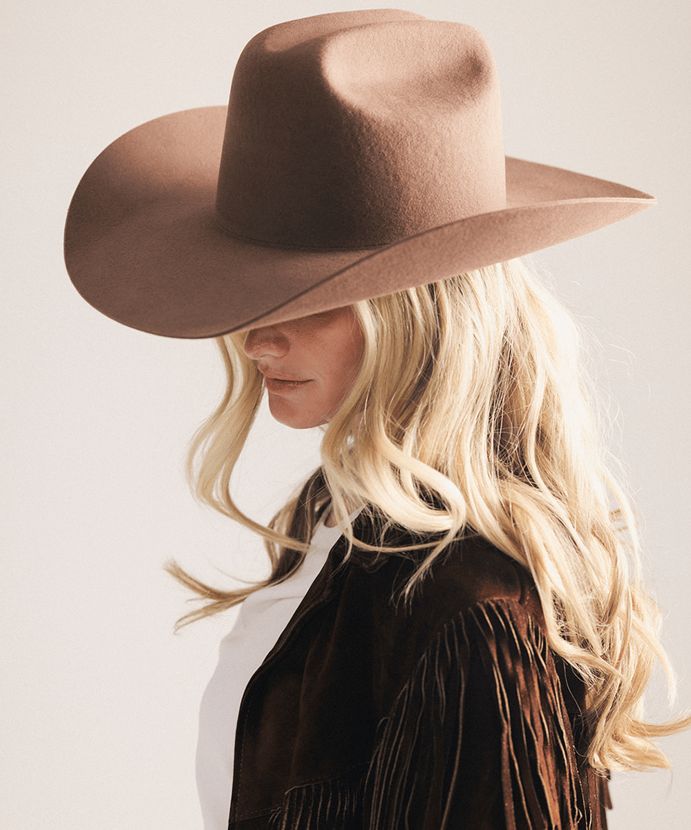 Woman wearing a brown cowboy hat and fringed jacket on a plain background #color_chocolate