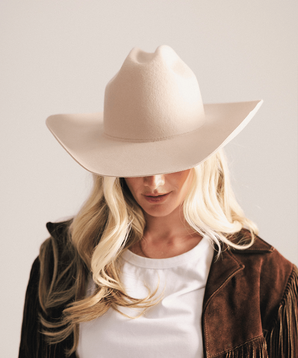 Woman wearing a beige cowboy hat and brown jacket on a light background #color_cream