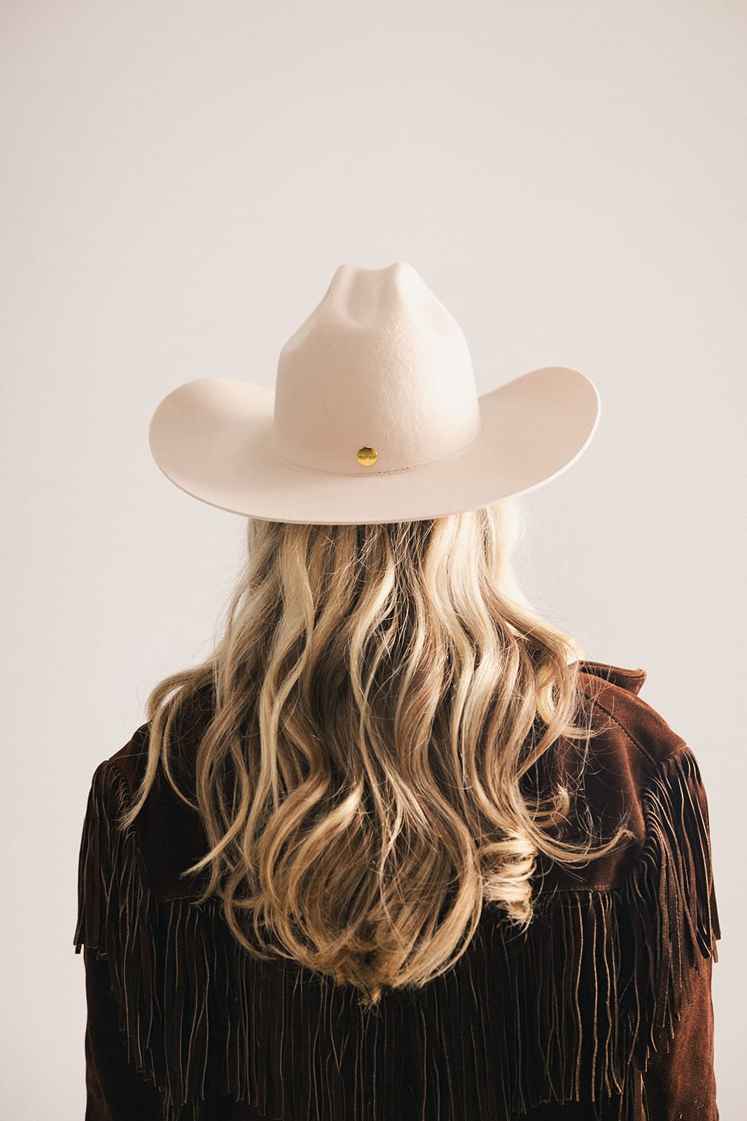 Woman wearing a beige cowboy hat and brown jacket on a light background #color_cream