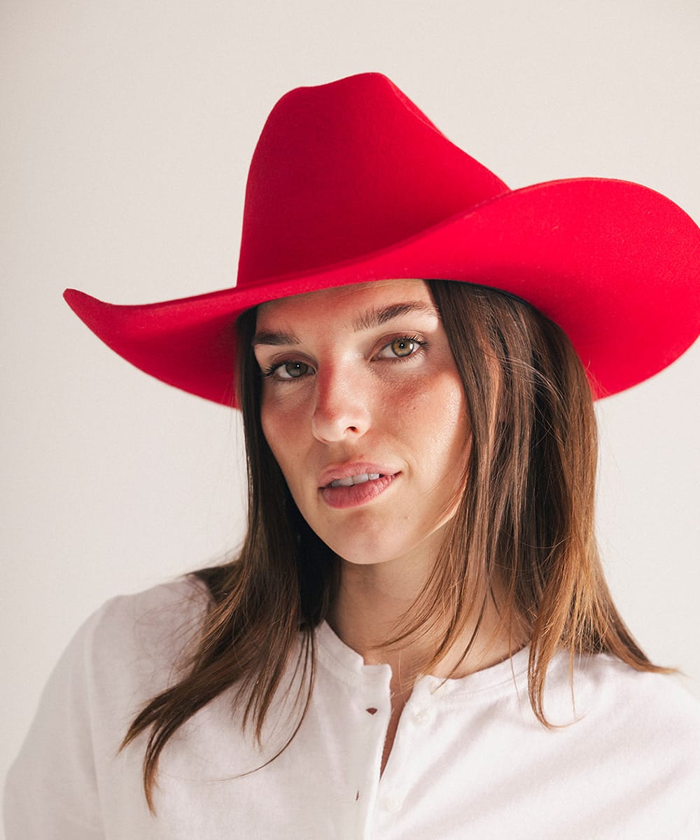 Woman wearing a red cowboy hat against a plain background #color_cherry red