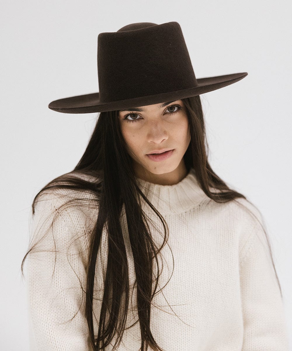 Woman wearing a dark brown gambler hat and a white sweater against a plain background #color_dark brown