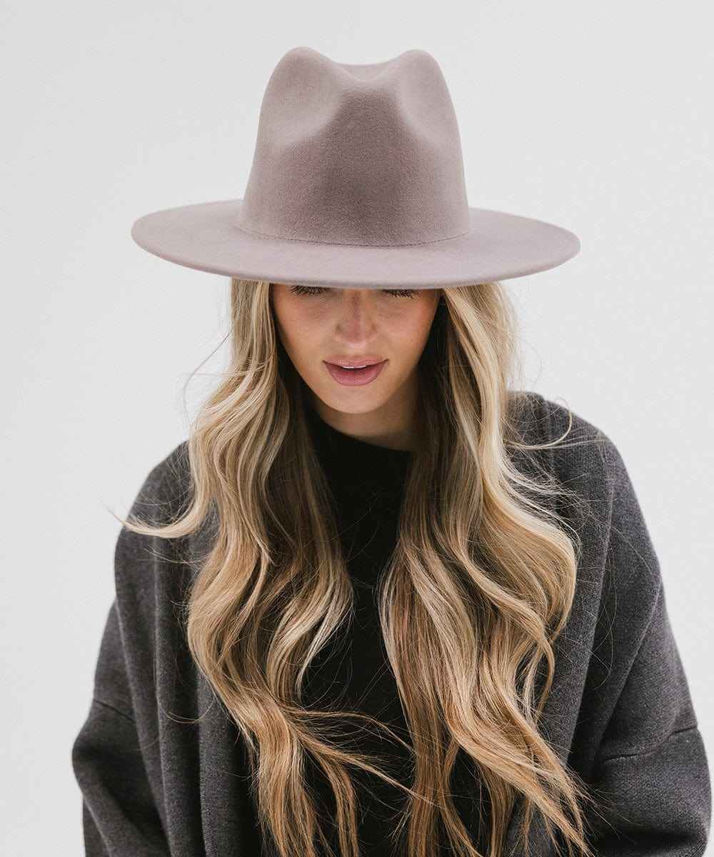 Woman wearing a light grey fedora hat and a dark grey jacket against a plain background #color_light grey