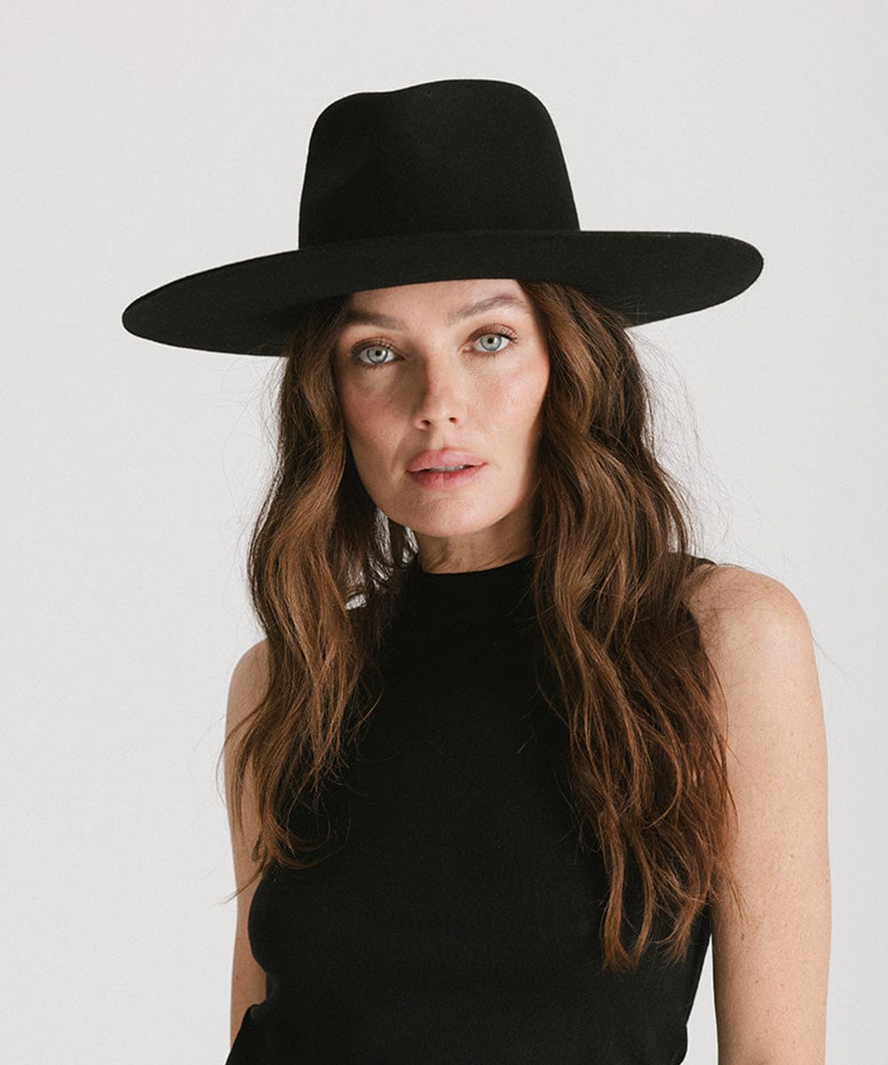 Woman wearing a black fedora hat and a black top against a plain background #color_black