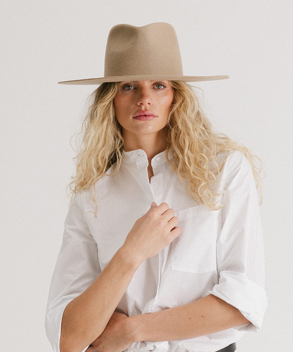 Woman wearing a tan fedora hat and a white shirt against a plain background #color_tan