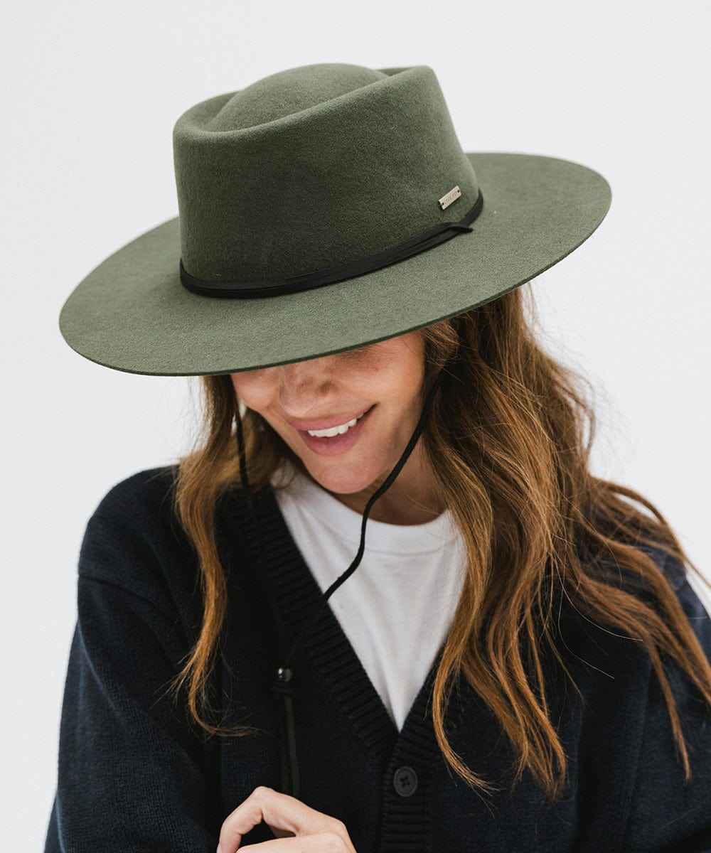 Woman wearing a green fedora hat with a hat band and a dark blue sweater against a plain background #color_green