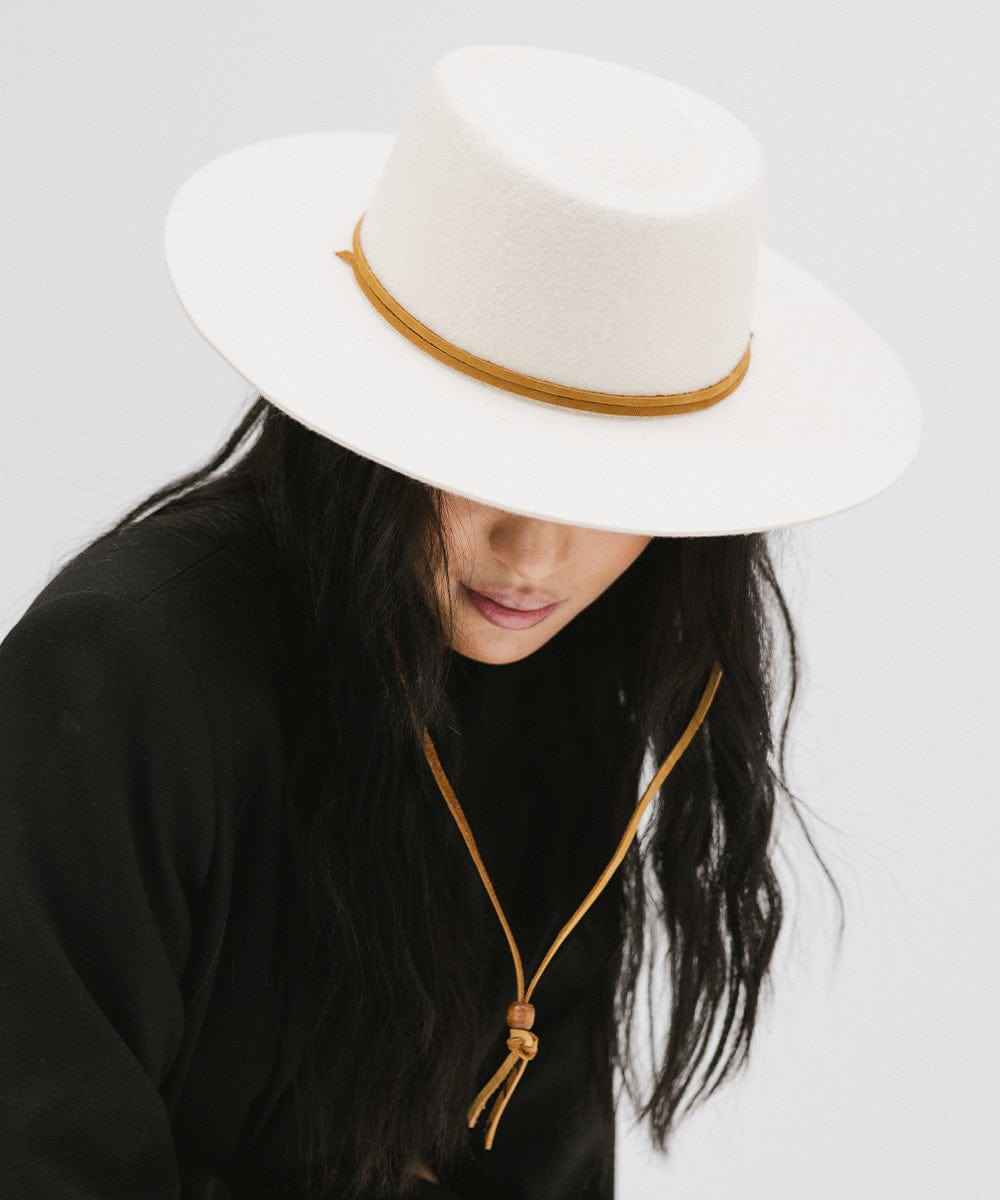 Woman wearing an off white wide-brimmed hat with a strap and a black coat against a plain background #color_off white