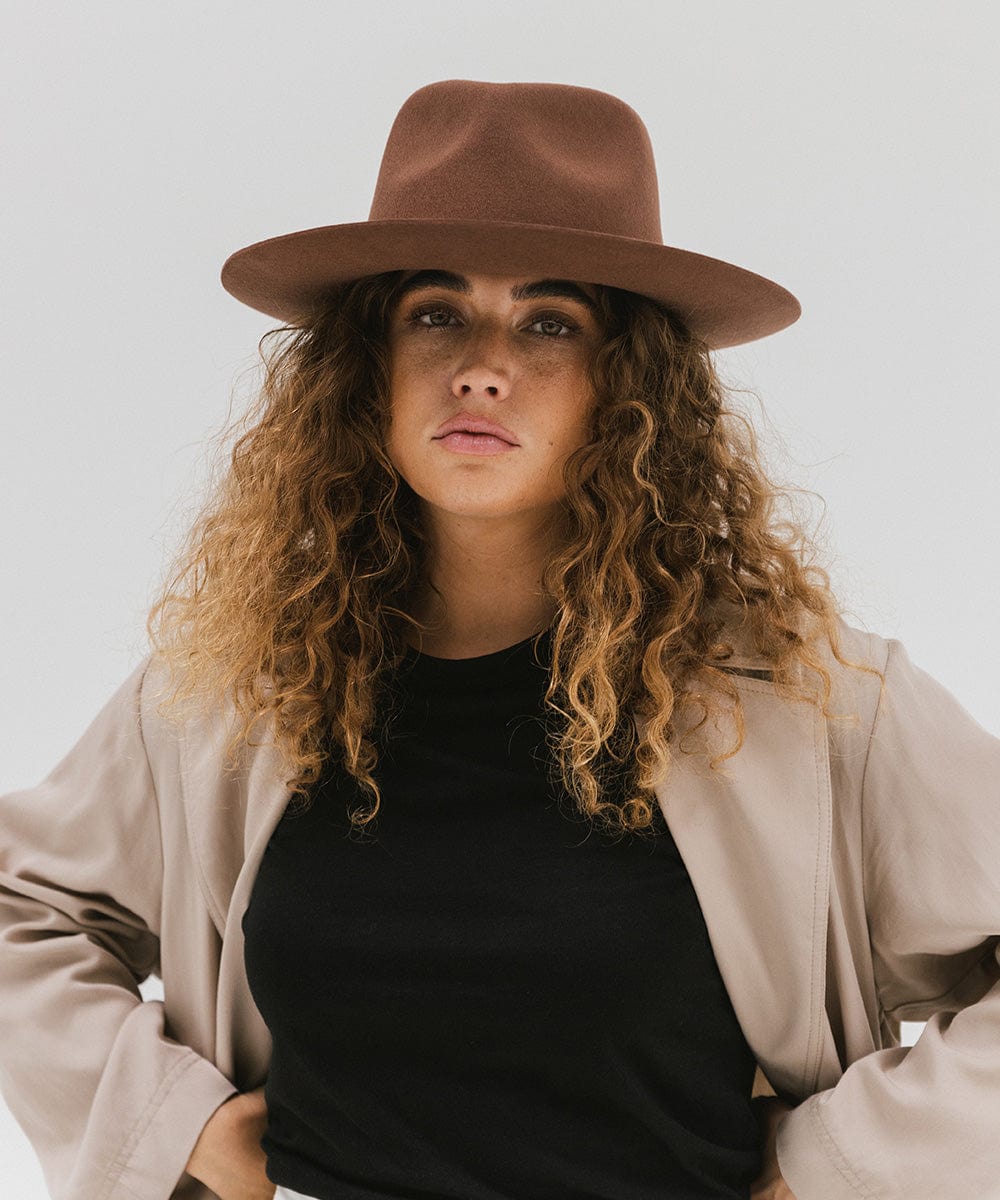 Woman wearing a dark oak colored fedora hat and black shirt with a beige jacket against a white background #color_dark oak
