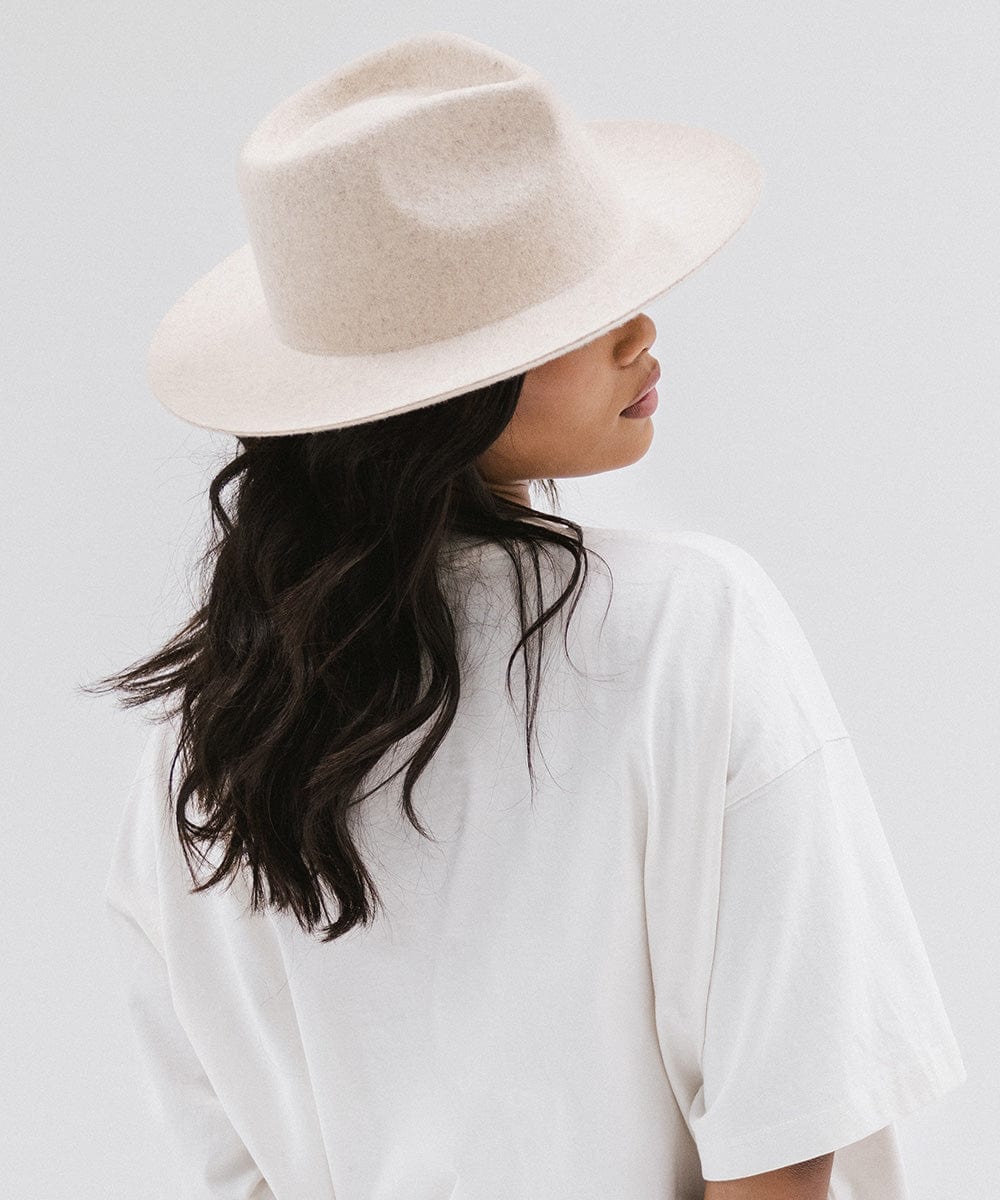 Woman wearing a mix ivory colored fedora hat and a white shirt, facing sideways against a white background #color_mix ivory