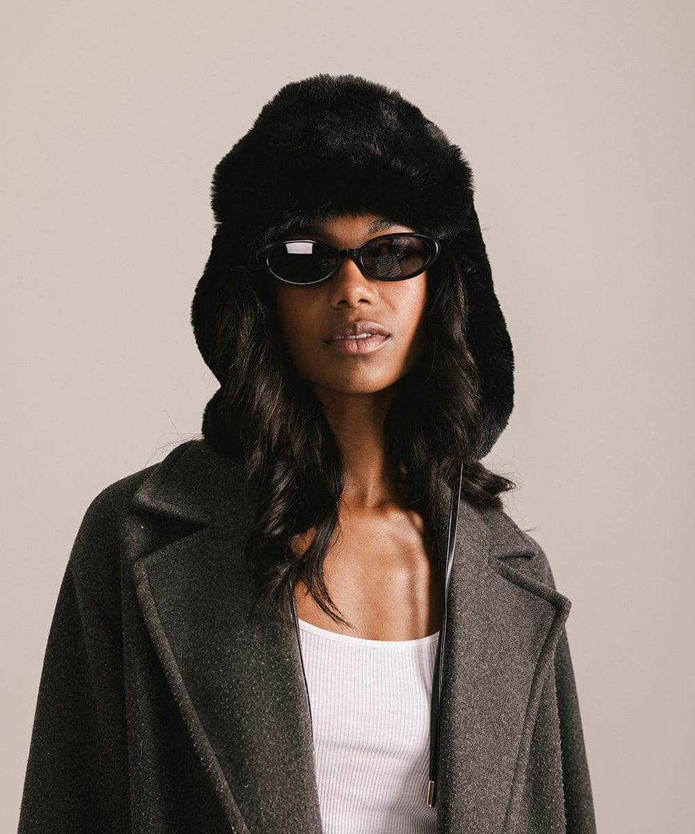 Woman wearing a black fur hat and gray coat against a beige background #color_black