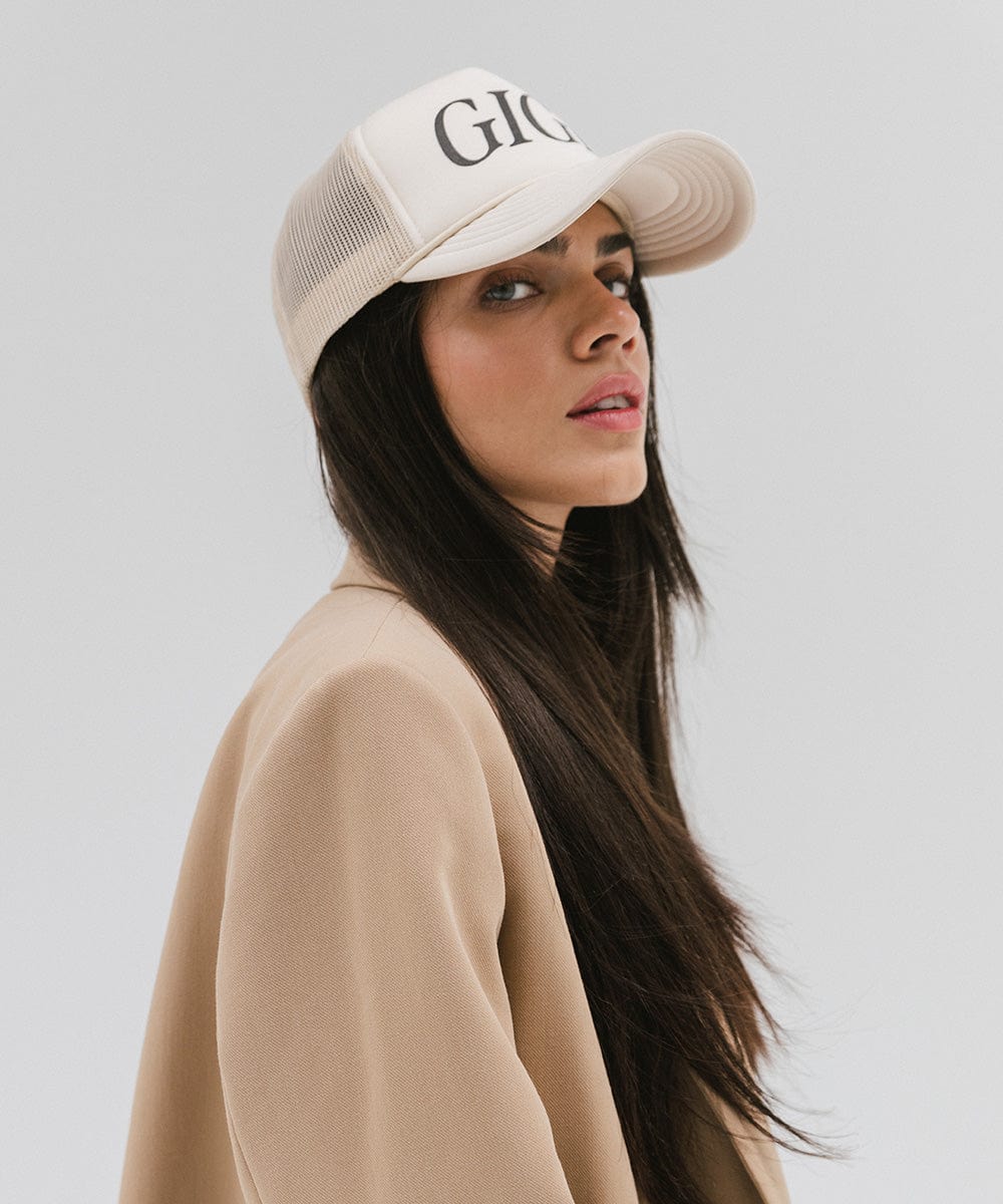 Woman wearing a cream cap with 'GIGI' text and a beige coat, posing sideways against a plain background #color_cream
