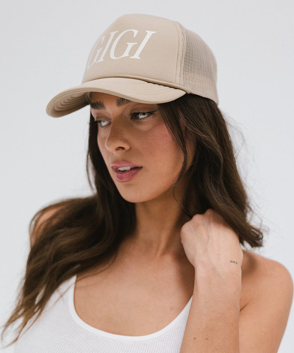 Woman wearing a tan cap with 'GIGI' text and a white top against a plain background #color_tan