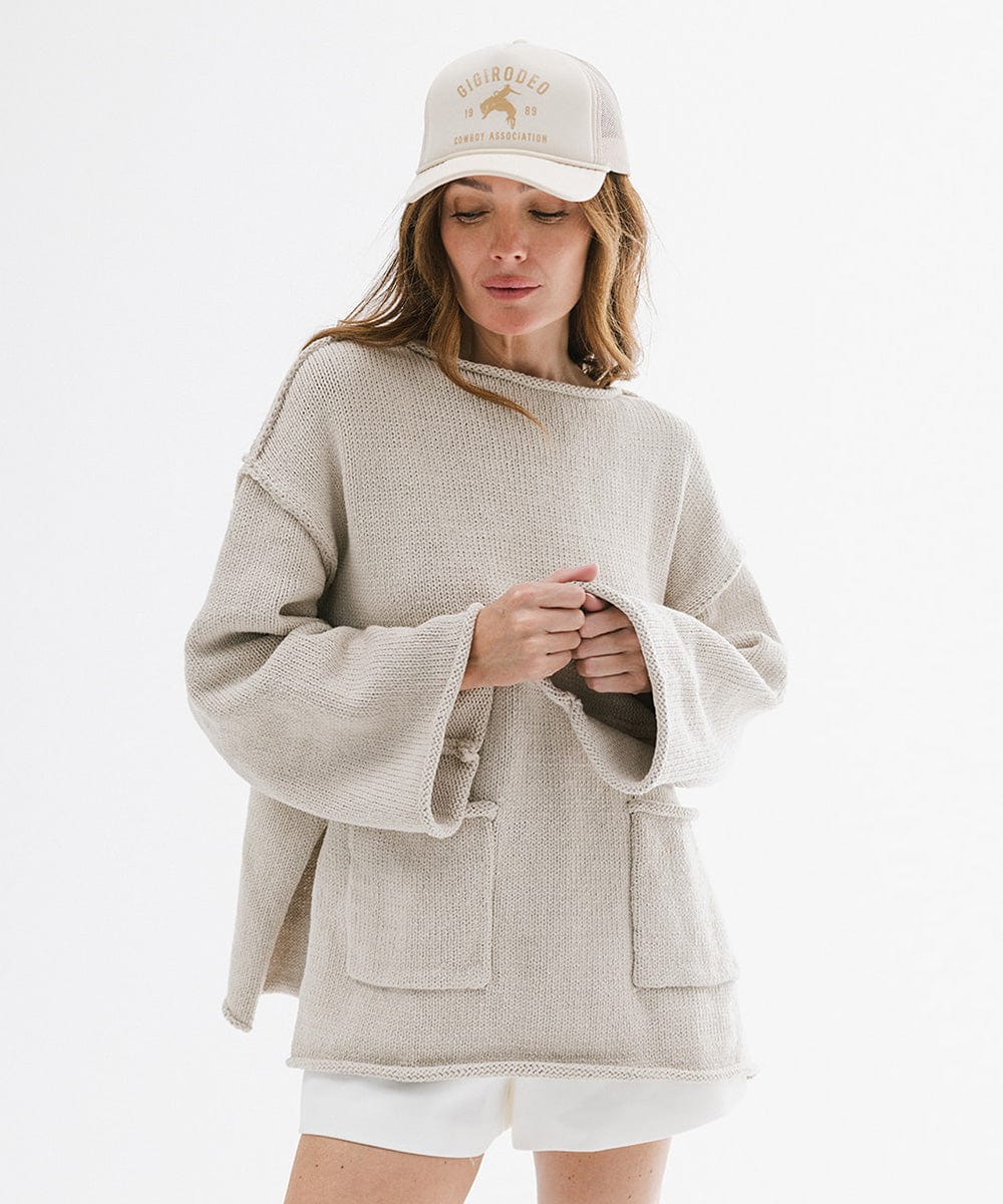 Woman wearing a cream cap with golden 'GIGIRODEO' text and logo, and a grey sweater and white shorts against a plain background #color_cream