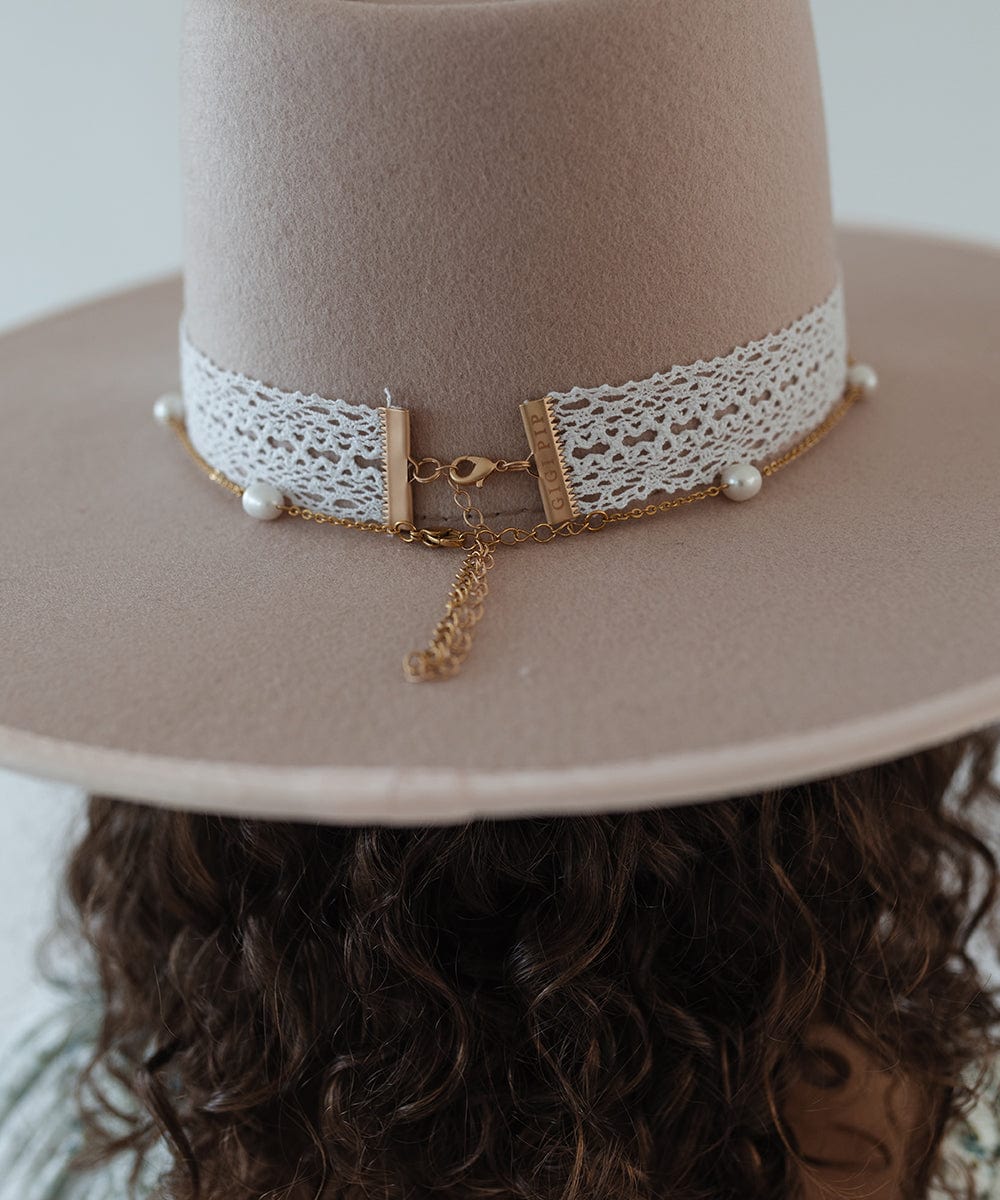 Person wearing a beige hat with a white band and a gold pearl chain band on a plain background #color_gold