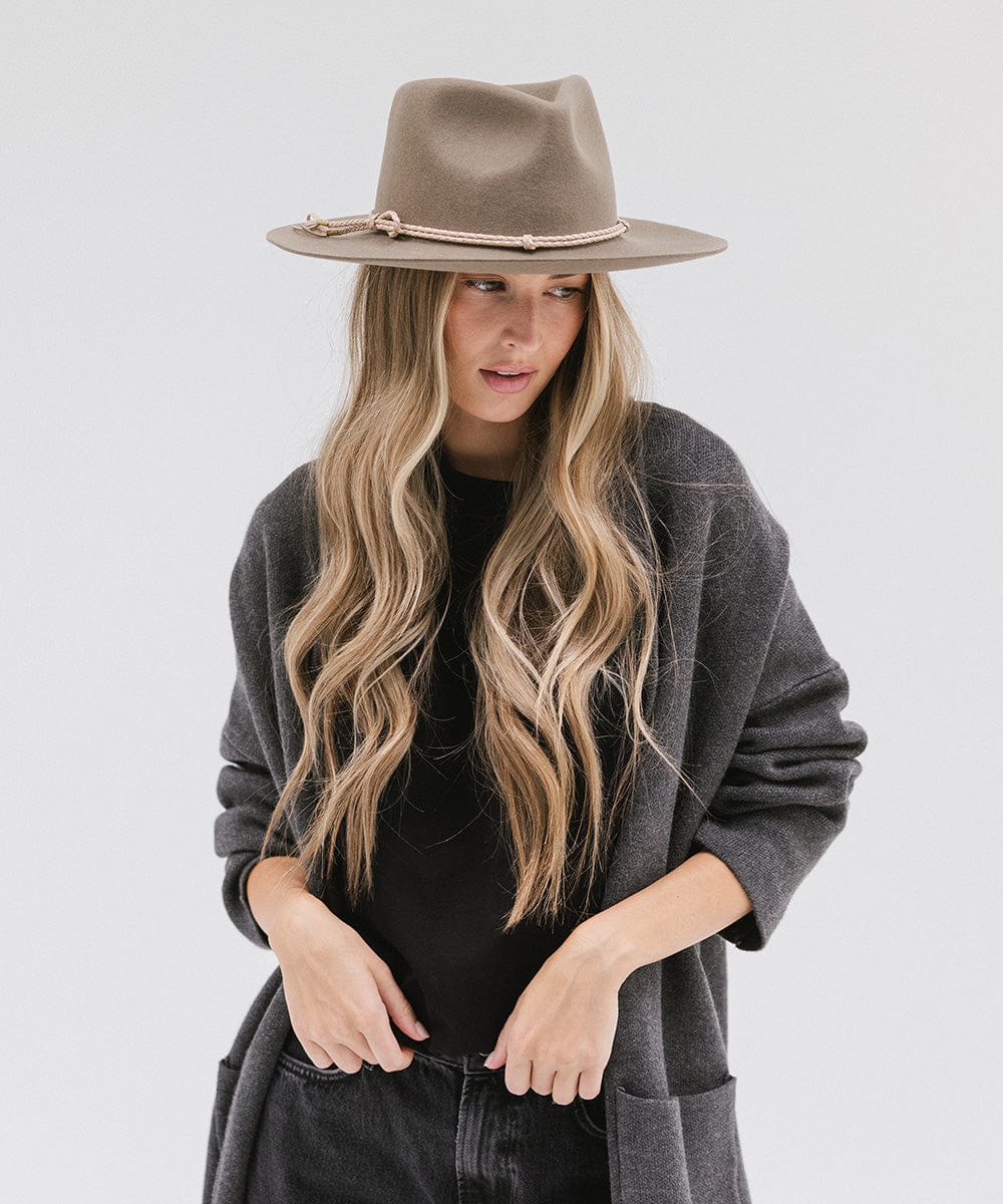 Woman wearing cowboy hat with a beige lasso braided hat band and a black t-shirt with grey jacket, posing against a plain background #color_cream