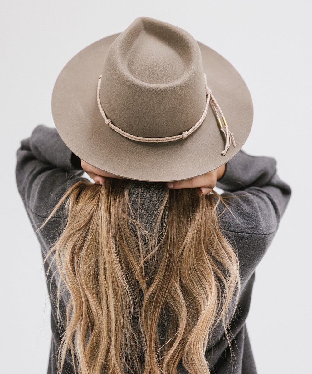 Person with long hair wearing cowboy hat with a beige lasso braided hat band and a grey sweater against a plain background #color_cream
